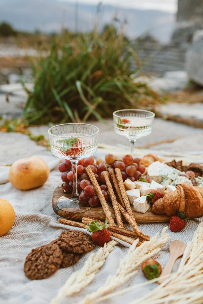 Charming picnic spread with wine glasses, cheese, grapes, and snacks in a rustic outdoor setting.