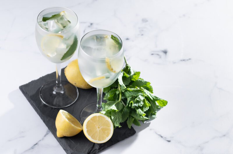Hugo Cocktail with Lemon, Mint, and Ice in a Wine Glass on marble background