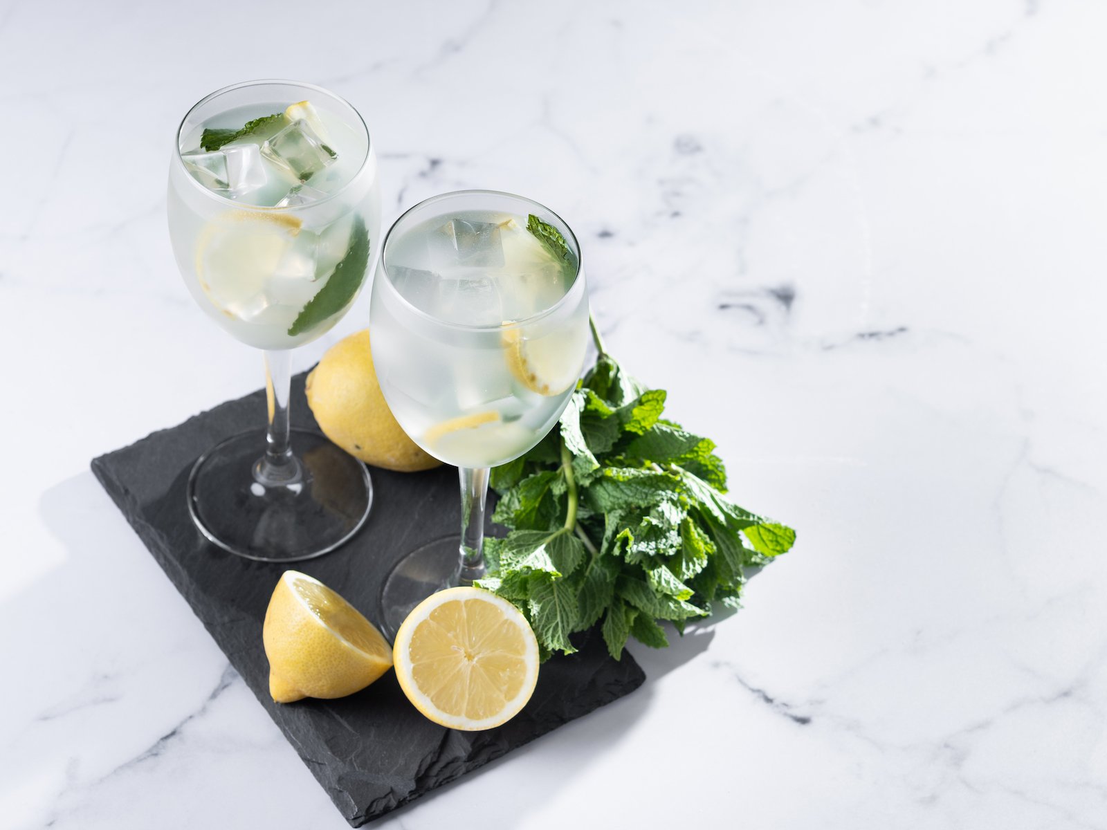 Hugo Cocktail with Lemon, Mint, and Ice in a Wine Glass on marble background